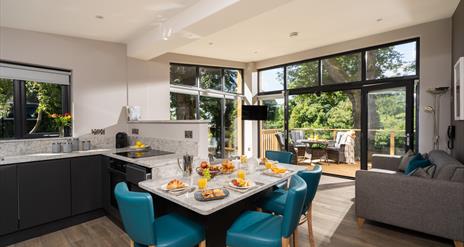 Open plan kitchen and dining area with view of lounge and outside area in background. Open patio doors floor to ceiling leading onto decked patio area