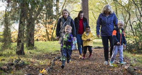 Boy, in Halloween costume,  running along autumn trail with family