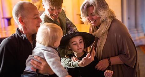 Family with girl dressed as a witch, smiling at a phone.