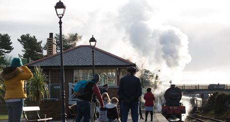 Steam train departing from Whitehead Station with family onlooking from platform