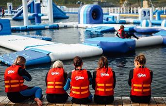 Image shows children wearing life jackets, sitting on the edge of the lake