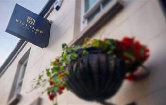 sign for Hillyard Huse on outside wall with hanging flower basket below.