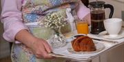 A tray being carried with coffee, orange juice and croissant.