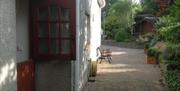 A paved outdoor area with a Dutch door, bench and lots of plants.