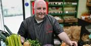 a man stands with a box filled with fresh vegetables including carrots, parsnips, celery, onions and cabbage