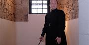 The female jailer is dressed in a long black dress from 1800's and holds a large brass key in the stone walled ceiling with bars on the window of the