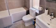 Tiled bathroom with bath/shower, toilet and a sink with a mirror.
