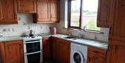 A kitchen with wooden cabinets, a double oven/hob, sink, microwave and a window.