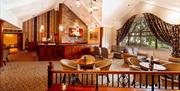Carpeted reception area with a wooden reception desk, a seating area with tables and chairs and a large window.
