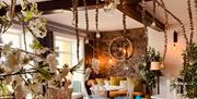Restaurant with tables and chairs decorated with faux plants and lamps.