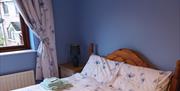 A double bedroom with blue walls, a bedside table and a window.