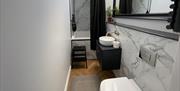 Marble bathroom with a toilet, sink, bath/shower and a large mirror.