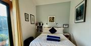 Bedroom with double bed, pictures on the walls. Floor to ceiling window overlooking garden.