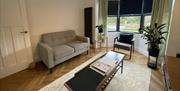 Living room with sofa, chair, coffee table, indoor plants and a large window with a lawn view.