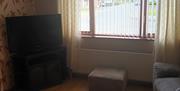 A living room with a TV, chair, footstool and a window.