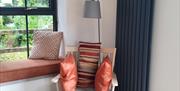 A seat with cushions beside a window seat with a lamp.