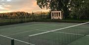A tennis court with a view of the countryside beside a large tree.