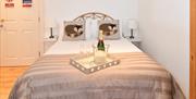 Double bed with bottle of champagne in an ice bucket sitting on tray positioned at the bottom of the bed