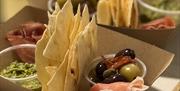 A selection of meats, cheeses, olives and a side of pesto.