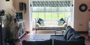 A tiled living room with a corner couch, a TV and a large window seat with a garden view.