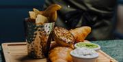 fish and chips with condiments in ramakins on the side, served on a wooden platter