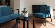 A living room with a teal coloured sofa and chair and a coffee table with a potted sitting on the table.