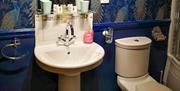 A blue wallpapered bathroom with a sink and toilet.