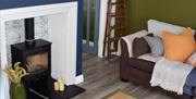 Living room with black wood burning stove situated within a blue chimney breast and tiled alcove, brown sofas with yellow, blue. green and orange acce
