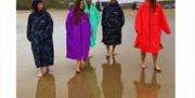 a group of 5 people wear dry robes on the beach