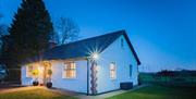 A cottage at night beside a country feild in front of a large tree.