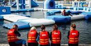 Image shows children wearing life jackets, sitting on the edge of the lake