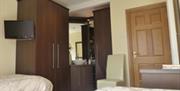 A bedroom with two beds, a chair, TV and a large corner wardrobe with a mirror.
