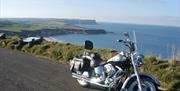 A Harley-Davidson on a road overlooking cliffs with a beach.