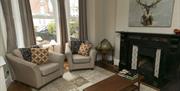 A living room with two chairs, a coffee table, a fireplace, a globe and a painting of a deer.