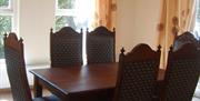 A wooden table and chairs in a dining room with windows.