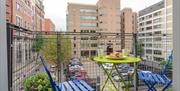 A balcony with garden furniture overlooking a car-park.