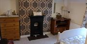 A bedroom with wallpaper, drawers, a mirror and a small fireplace.