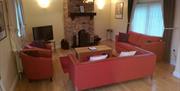 Image shows lounge area with sofas, chairs, TV and fireplace. Two windows in the room.