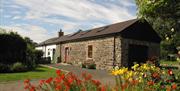 Converted cobblestone barn in the country with red and yellow flowers.