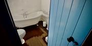 A blue door leading to a bathroom with a toilet, bath and sink.