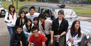 A group of tourists laughing with a black taxi.