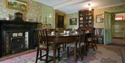 A historic dining room with a table, cupboard, paintings and a large fireplace.