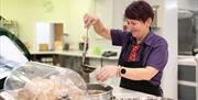 Image shows woman ladling soup into a container in the cafe