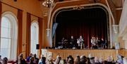 a band performs on stage at Portrush Town Hall while seated crowds watch