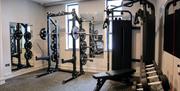 Photo of the mini gym in the Holiday Inn Express Belfast City. There are weights on a rack in the foreground, two weightlifting benches/stations in th