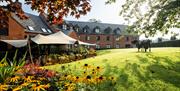 exterior view of Coq & Bull brasserie terrace and hotel gardens with a covered awning over dining area.