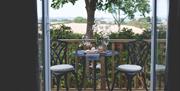 Outside sitting area with table and 2 chairs overlooking tree and shrubbery with field in the background.