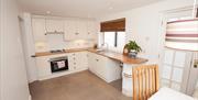 A white kitchen with a hob/oven, a sink and a back patio door.