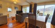 An open plan dining room with a table and chairs, large windows and a living room area.