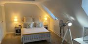 Image shows double bedroom with floor fan and floor light, beside tables and lamps